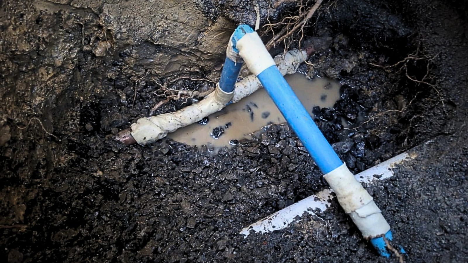 Excavated trench exposing a blue water pipe with taped joints during a Napier leak repair